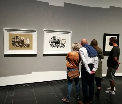 Joukko näyttelyvieraita Banksyn taidekauppakriittisen serigrafian edessä